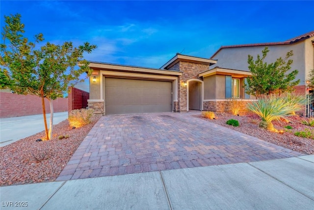 view of front facade featuring a garage, fence, stone siding, decorative driveway, and stucco siding