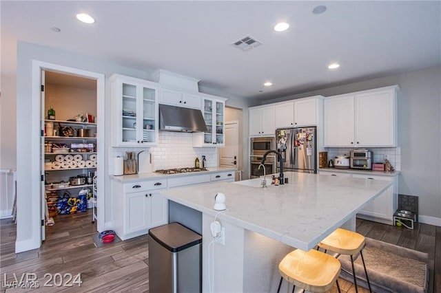 kitchen featuring appliances with stainless steel finishes, dark wood-type flooring, light stone countertops, white cabinets, and a kitchen island with sink