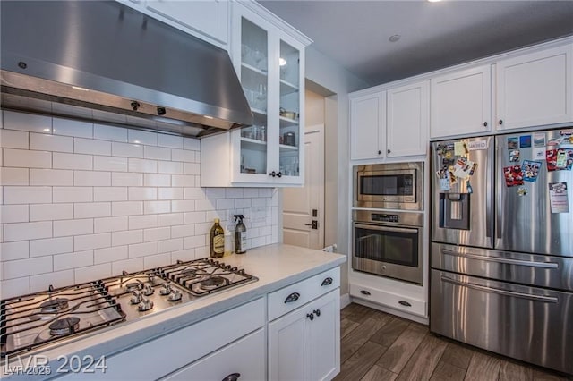 kitchen with stainless steel appliances, white cabinets, ventilation hood, backsplash, and dark hardwood / wood-style flooring