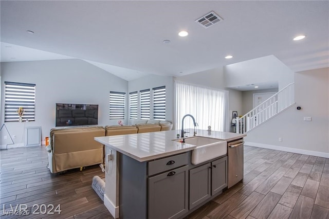 kitchen featuring stainless steel dishwasher, vaulted ceiling, gray cabinets, sink, and a kitchen island with sink