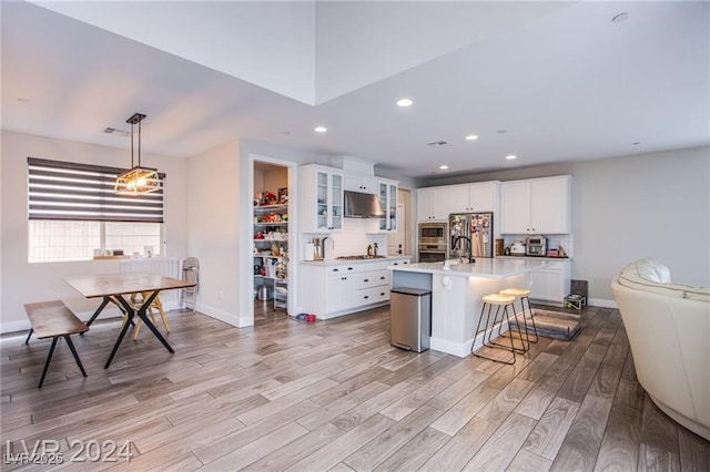 kitchen featuring white cabinetry, a center island with sink, light wood-type flooring, stainless steel appliances, and pendant lighting