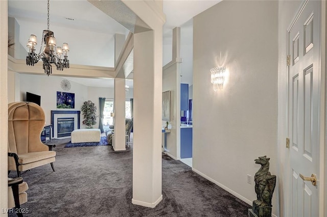 interior space featuring a chandelier, dark colored carpet, a glass covered fireplace, and baseboards