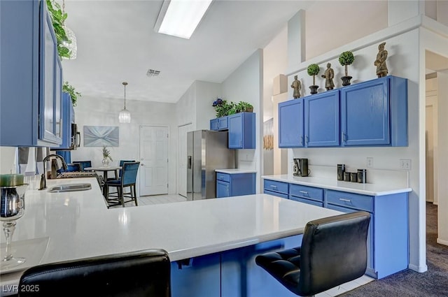 kitchen featuring blue cabinets, a peninsula, a sink, light countertops, and a kitchen bar