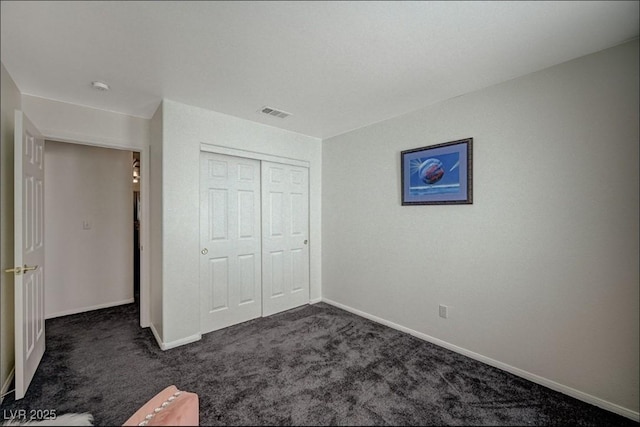 unfurnished bedroom with a closet, visible vents, dark carpet, and baseboards