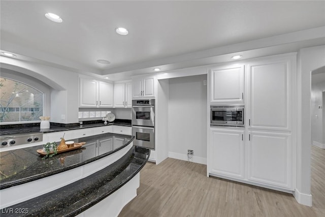 kitchen with light wood finished floors, recessed lighting, appliances with stainless steel finishes, white cabinetry, and dark stone countertops