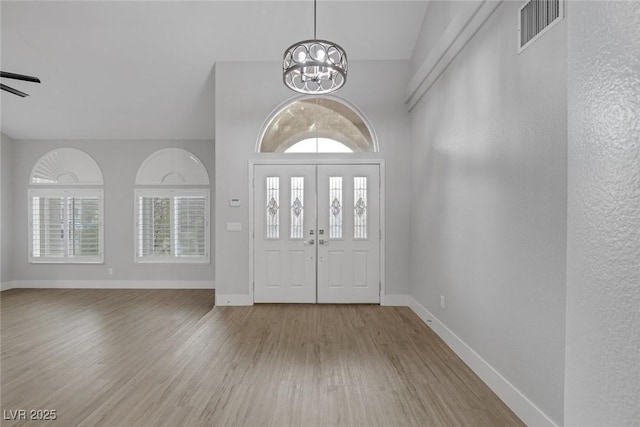 foyer entrance with ceiling fan with notable chandelier, visible vents, baseboards, and wood finished floors