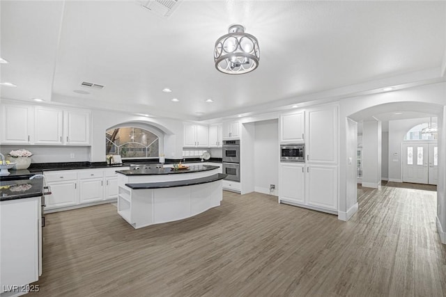 kitchen with arched walkways, appliances with stainless steel finishes, visible vents, and white cabinets