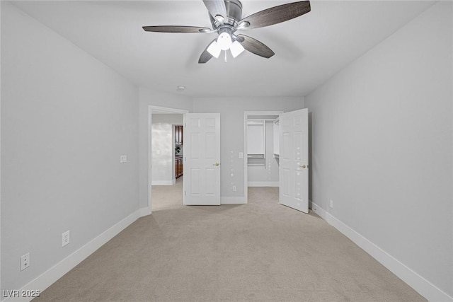 unfurnished bedroom featuring baseboards, a ceiling fan, light colored carpet, a walk in closet, and a closet