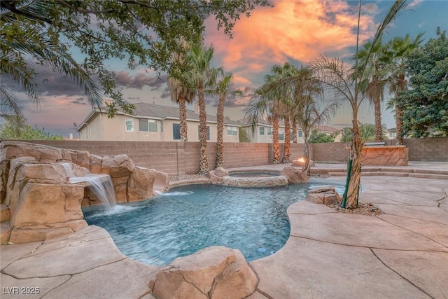 pool at dusk with a fenced backyard, a pool with connected hot tub, and a patio