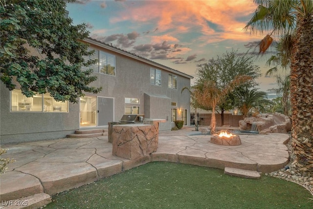 rear view of property featuring an outdoor fire pit, a patio, an outdoor kitchen, and stucco siding