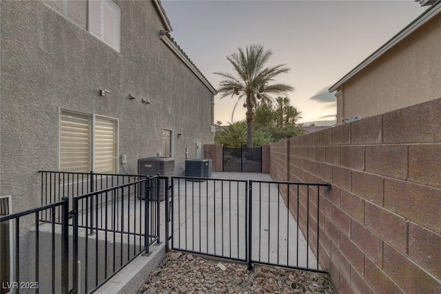 patio terrace at dusk featuring cooling unit, a gate, and fence