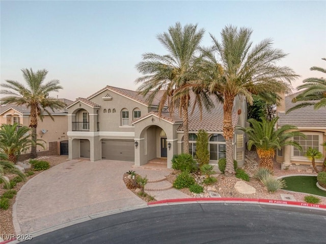 mediterranean / spanish house featuring decorative driveway, a tiled roof, an attached garage, and stucco siding