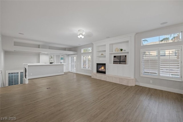 unfurnished living room featuring a tiled fireplace, wood finished floors, visible vents, and baseboards