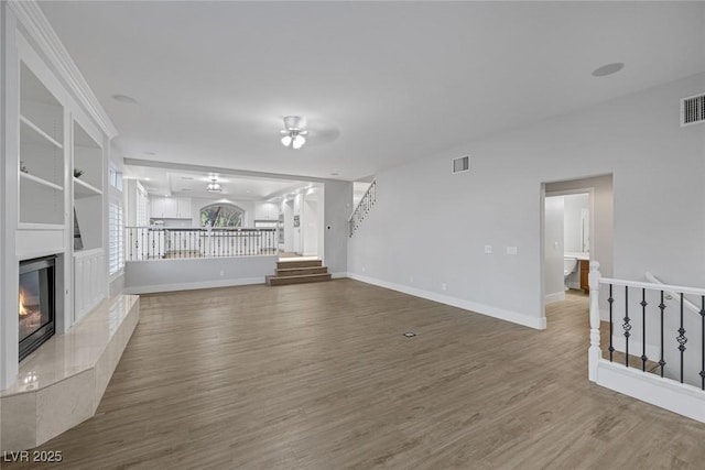 unfurnished living room with stairway, visible vents, wood finished floors, and a high end fireplace