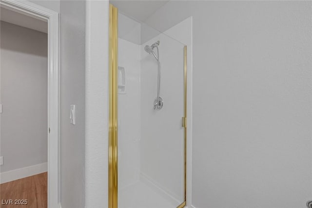 bathroom with wood finished floors, a shower stall, and baseboards