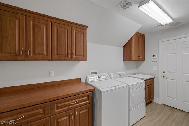 clothes washing area featuring cabinet space, visible vents, washer and clothes dryer, light wood-style flooring, and a sink