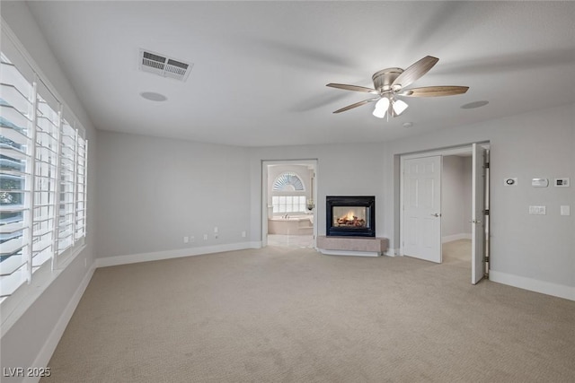 unfurnished living room featuring light colored carpet, visible vents, a ceiling fan, a multi sided fireplace, and baseboards