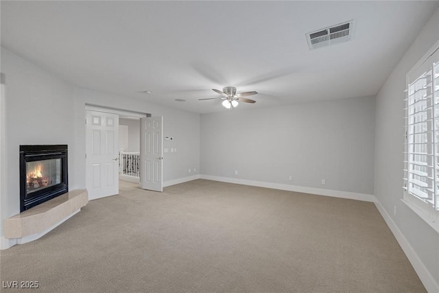 unfurnished living room with light colored carpet, a ceiling fan, visible vents, baseboards, and a glass covered fireplace