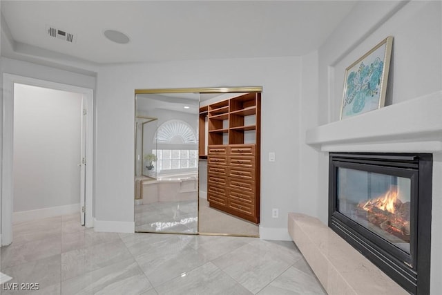 unfurnished living room featuring baseboards, visible vents, and a glass covered fireplace