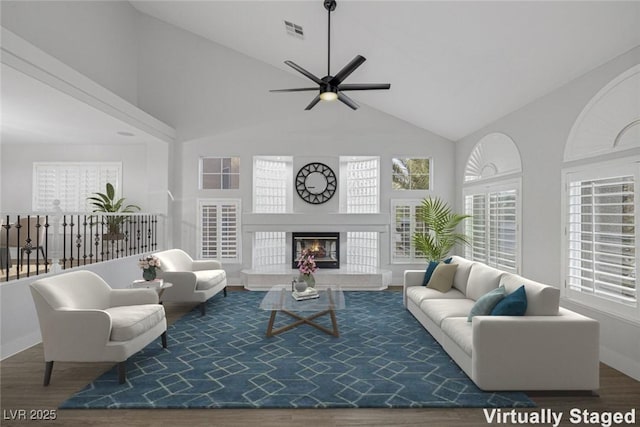 living room featuring high vaulted ceiling, a glass covered fireplace, visible vents, and wood finished floors