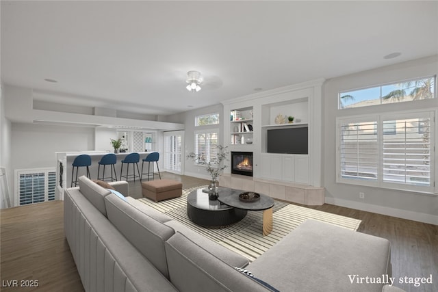 living area featuring built in features, visible vents, a tiled fireplace, wood finished floors, and baseboards