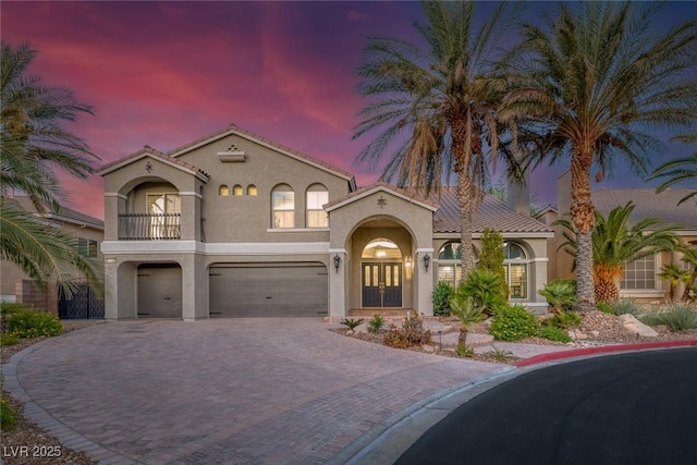 mediterranean / spanish-style house with an attached garage, stucco siding, decorative driveway, and french doors