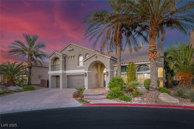 mediterranean / spanish home with decorative driveway, stucco siding, an attached garage, a balcony, and a tiled roof