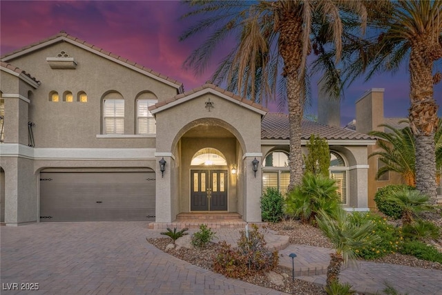 mediterranean / spanish house featuring a tile roof, an attached garage, decorative driveway, french doors, and stucco siding