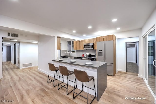 kitchen with a kitchen bar, light hardwood / wood-style floors, stainless steel appliances, kitchen peninsula, and decorative backsplash