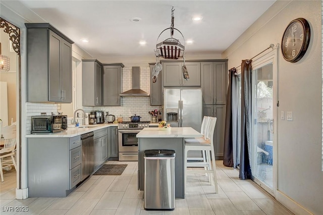 kitchen featuring appliances with stainless steel finishes, wall chimney range hood, gray cabinetry, and a center island