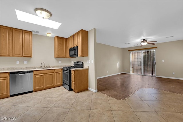 kitchen with a skylight, black appliances, ceiling fan, light tile patterned floors, and sink