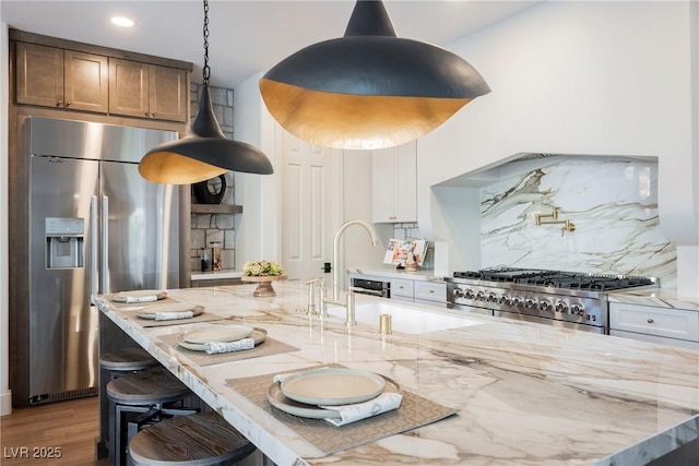 kitchen with stainless steel built in refrigerator, range, light stone counters, white cabinets, and backsplash