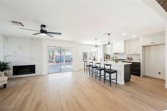 kitchen featuring tasteful backsplash, decorative light fixtures, light wood-type flooring, white cabinetry, and a kitchen island with sink