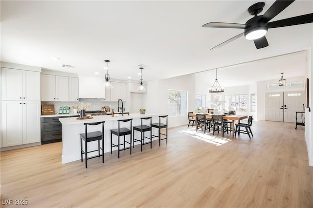 kitchen with sink, white cabinetry, pendant lighting, a kitchen island with sink, and tasteful backsplash