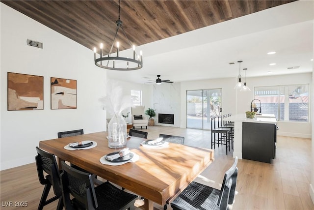 dining space featuring light wood-type flooring, a high end fireplace, sink, wooden ceiling, and ceiling fan with notable chandelier