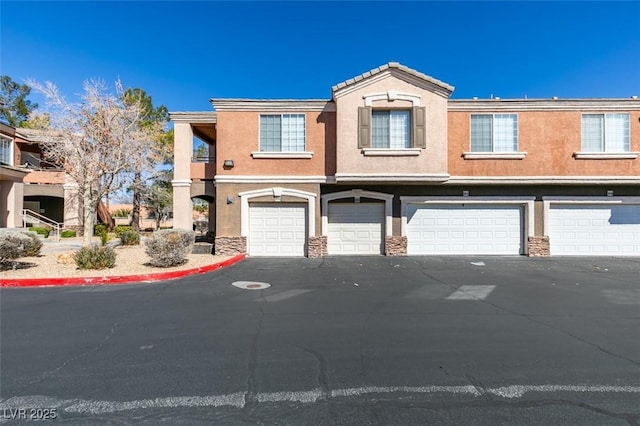 multi unit property featuring a garage, stone siding, and stucco siding