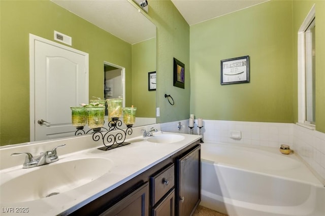 bathroom featuring a bath, double vanity, a sink, and visible vents