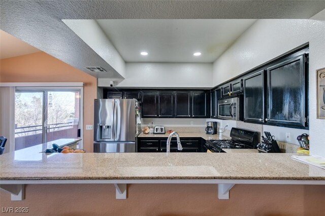 kitchen with appliances with stainless steel finishes, dark cabinetry, a peninsula, and a kitchen bar