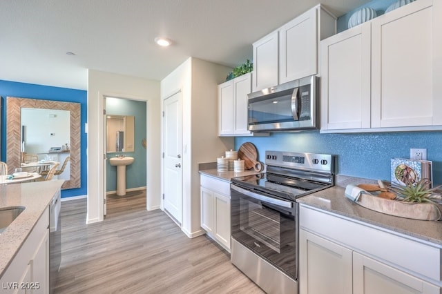 kitchen with white cabinetry, light wood-type flooring, stainless steel appliances, sink, and light stone counters