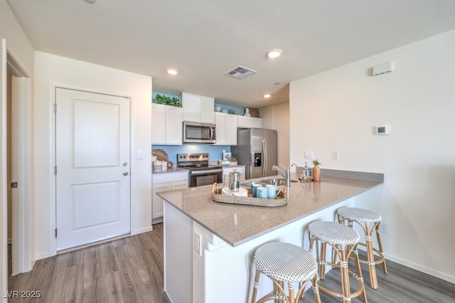 kitchen featuring white cabinetry, a kitchen breakfast bar, stainless steel appliances, kitchen peninsula, and light stone countertops