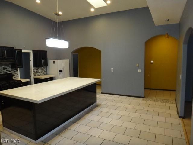 kitchen featuring arched walkways, light countertops, hanging light fixtures, dark cabinets, and white fridge with ice dispenser