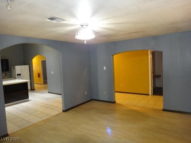 empty room featuring arched walkways, light wood finished floors, and visible vents