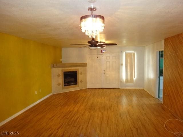 unfurnished living room with ceiling fan with notable chandelier, a fireplace, baseboards, and wood finished floors