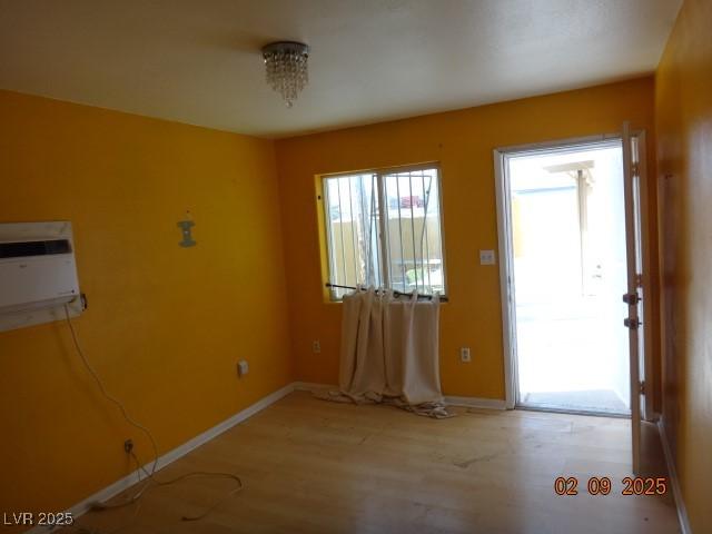 foyer entrance with a wall unit AC, light wood-style floors, and baseboards