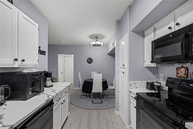 kitchen with light hardwood / wood-style floors, white cabinetry, black appliances, and light stone counters