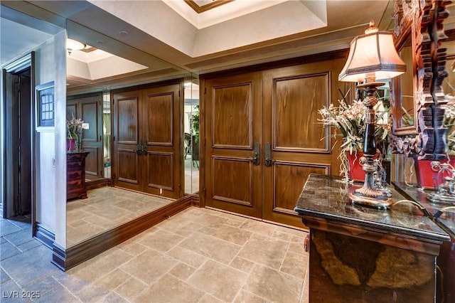 foyer entrance featuring stone tile floors, a tray ceiling, and crown molding