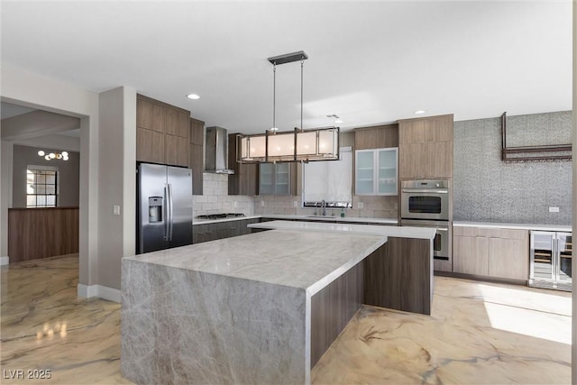 kitchen featuring a chandelier, stainless steel appliances, a center island, wall chimney exhaust hood, and modern cabinets