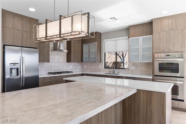 kitchen with decorative backsplash, wall chimney exhaust hood, modern cabinets, appliances with stainless steel finishes, and a sink