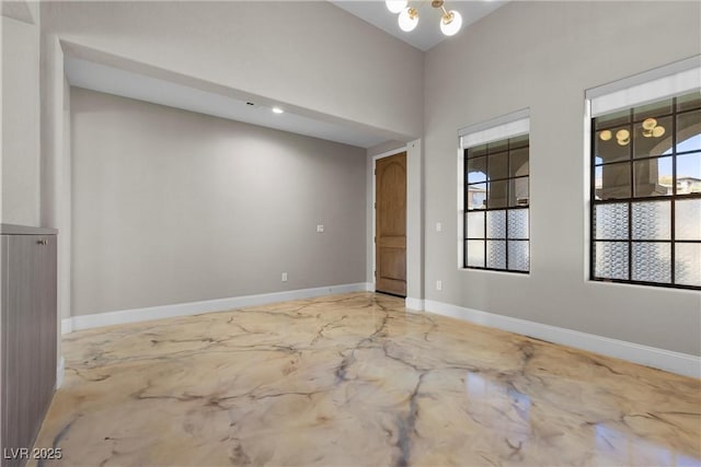 spare room with a chandelier, marble finish floor, a healthy amount of sunlight, and baseboards