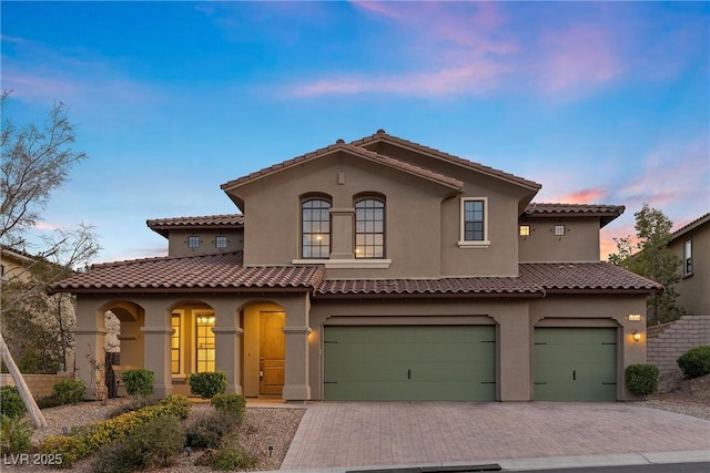 mediterranean / spanish-style house featuring a garage, a tiled roof, decorative driveway, and stucco siding